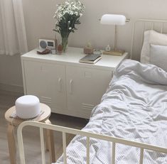 a white bed sitting next to a nightstand with flowers on it