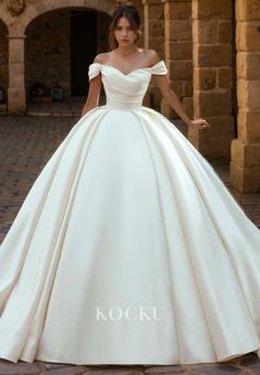 a woman in a white wedding dress standing on a brick walkway with her hands behind her back