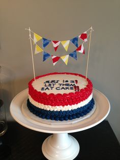 a red, white and blue cake sitting on top of a table with bunting