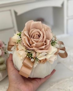 a hand holding a white pumpkin with a flower on it's side and ribbon around the top