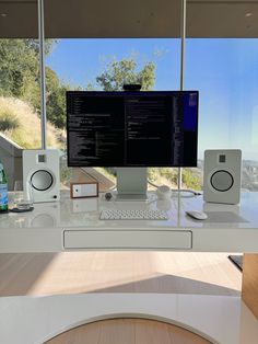 a computer monitor sitting on top of a desk in front of a large window next to a keyboard and mouse