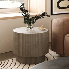 a vase with flowers on top of a table in front of a chair and window