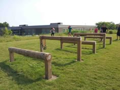 several people are standing in the grass near benches that have been made out of logs