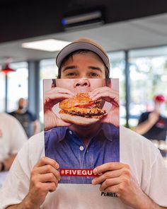 a man holding up a photo of himself eating a hamburger in front of his face