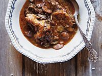 a white plate topped with meat and mushrooms covered in gravy next to a fork