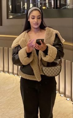 a woman standing in front of a building holding a cell phone and looking at it