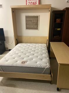 a bed frame with a mattress on it in a room next to a desk and tv