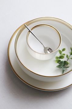 a white and gold plate with a silver fork on it, next to a small green plant