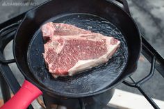 steak being cooked in a cast iron skillet on an outdoor stove top with red spatula