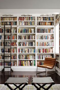 a living room filled with lots of books on top of a white book shelf next to a window