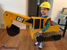 a young boy dressed up as a construction worker holding a large toy bulldozer