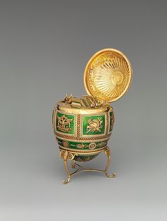 a green and gold box with a golden lid on it's stand in front of a gray background