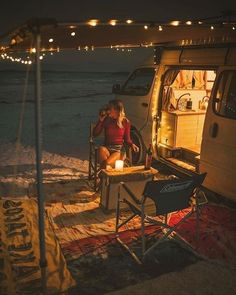 a woman sitting at a table in front of a camper van on the beach