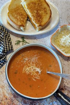 A bowl of creamy tomato soup with a grilled cheese sandwich in the background.