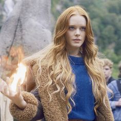 a woman with long red hair and blue shirt holding a fireball in her hand