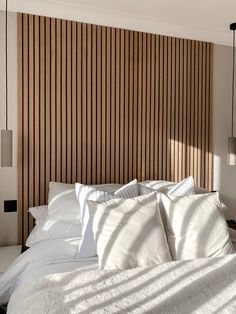 a bed with white sheets and pillows next to a wooden headboard that has vertical slats on it