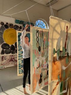 a woman is standing in front of some art on the wall with her hands up