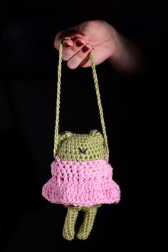 a hand holding a small crocheted toy in the shape of a frog with a pink dress