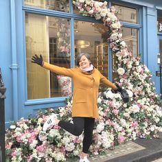 a woman is jumping in front of a flower display with her arms out and hands outstretched