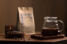 a wooden table topped with a bag of coffee next to a bowl of beans and a tea pot