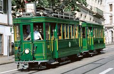 a green trolley car traveling down a street next to tall buildings