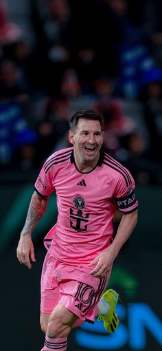 a male soccer player in a pink uniform is running with the ball and has his mouth open