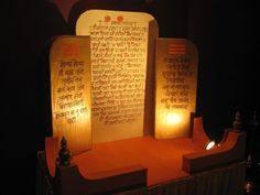 an illuminated display with two lit candles and some writing on the wall in front of it