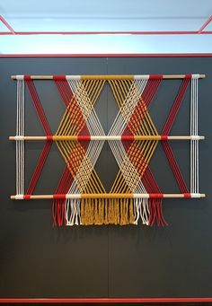 a wall hanging made out of woven material with red, yellow and white strips on it