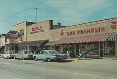 an old photo of cars parked on the side of the road in front of stores