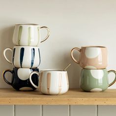 three coffee mugs sitting on top of a wooden shelf next to a white wall