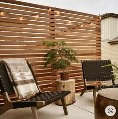 an outdoor patio with wooden slats and lights on the wall, potted plant in front of two chairs