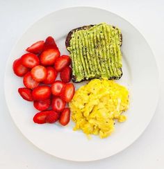 a white plate topped with toast, eggs and strawberries next to sliced avocado