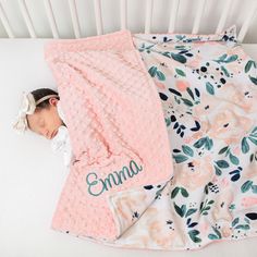 a baby wrapped in a pink blanket laying on top of a white crib next to a flowered blanket