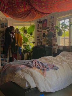 an unmade bed in a room with lots of plants and pictures on the wall