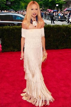 a woman in an off the shoulder dress on a red carpet with people standing around