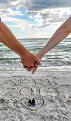 two people holding hands while standing in the sand at the beach with an i love you written on it