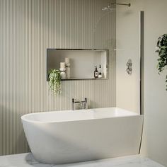 a white bath tub sitting next to a mirror in a bathroom under a light fixture