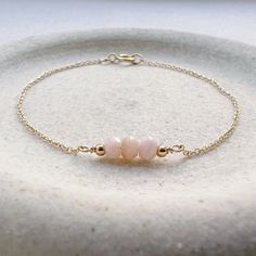 "Genuine pink opal birthstone beads and two tiny gold filled beads line a simple, minimalist, dainty chain in a choice of gold filled, 14k gold, rose gold filled, or sterling silver chain. Opal is the October birthstone. It is the perfect everyday bracelet and would make a special gift. We have birthstones for every month and other popular gemstones. * Sizing: 6\"- XXS/XS,  6.5\"/S, 7\"/M, and 7.5\"/L.  Bracelets come in 6\", 6.5\", 7\", and 7.5\". If you need a shorter or longer length please write that length in the 'notes to seller' section during checkout. CRAFTSMANSHIP  Jewelry is handmade by us in our NYC studio. We focus on craftsmanship and quality using only the highest quality materials and handpicked genuine gemstones.  PACKAGING We take pride in creating beautifully packaged or Dainty Gold Bracelet, Opal Birthstone, Everyday Bracelet, Beaded Jewlery, Silver Jewelry Design, Opal Bracelet, Birthstone Bracelets, Wedding Jewelry Bracelets, Pink Bracelet