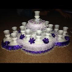 a purple and white wedding cake with many candles on the bottom tier, surrounded by lace