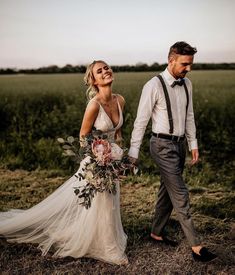 a bride and groom walking through a field