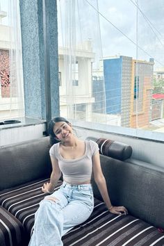 a woman sitting on top of a couch in front of a window next to a wall