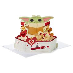 an origami baby yoda in a box with hearts on the bottom and eyes