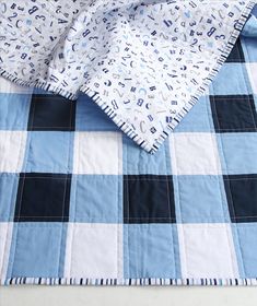 a blue and white checkered blanket on top of a bed with an unmade quilt