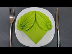 a white plate topped with a green leaf next to two silver forks and knifes