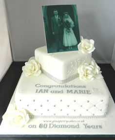 a wedding cake with white roses and an old photo on the top, sitting in front of a glass case