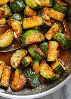 cooked zucchini and squash in a pan on a marble countertop with spoons