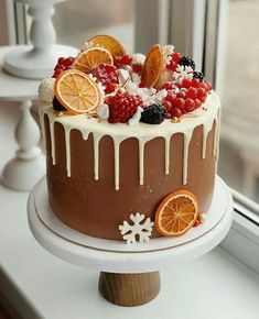 a chocolate cake with oranges, raspberries and blackberries on top sitting in front of a window