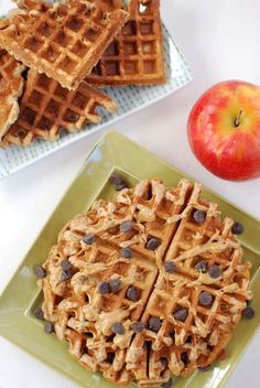 two plates with waffles and an apple next to them on a table top