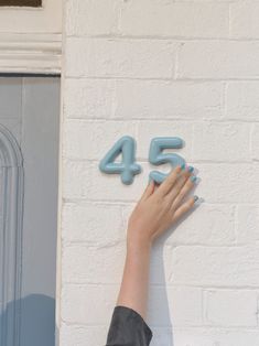 a woman's hand reaching up to the number 45 on a wall with blue nails