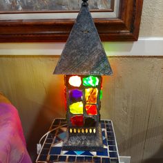 a stained glass lamp sitting on top of a night stand in front of a painting